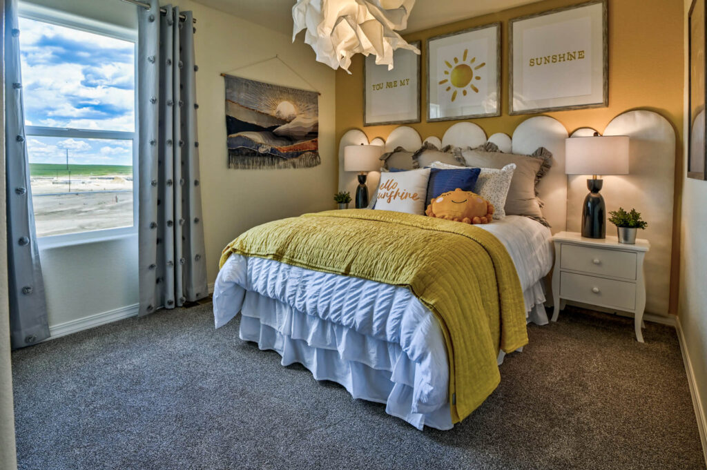 Bedroom with a yellow throw blanket, scalloped headboard, bedside tables, and window with curtains.