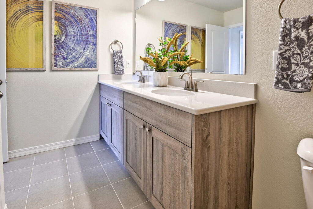 Bathroom vanity with double sinks, wood-tone cabinets, large mirror and decorative wall art.