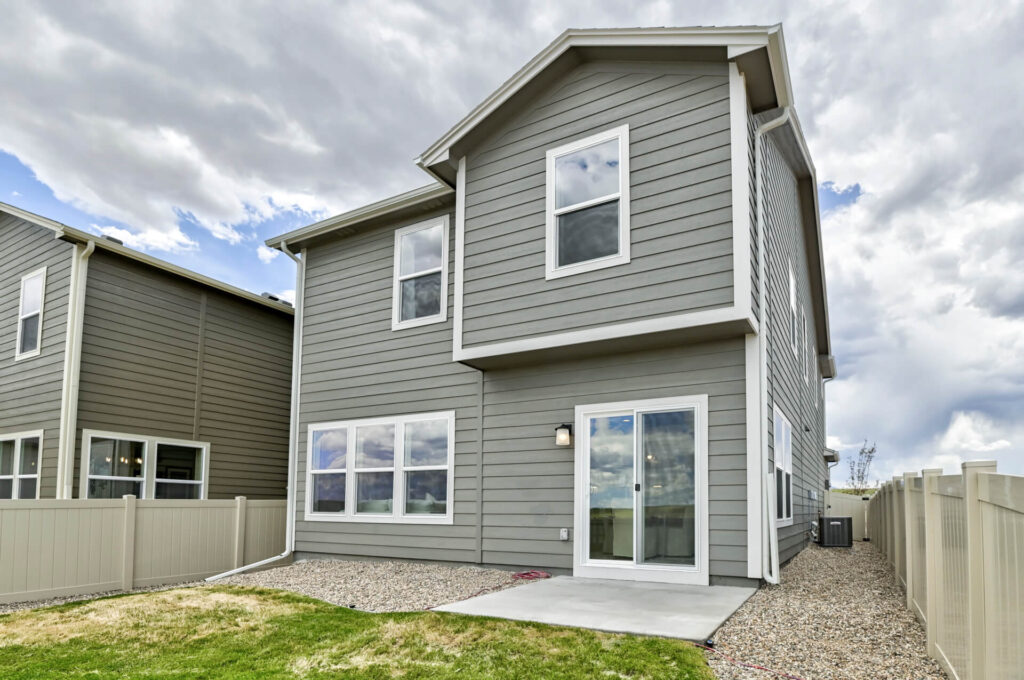 Rear exterior of a two-story gray house with sliding glass door, fenced yard and concrete patio.