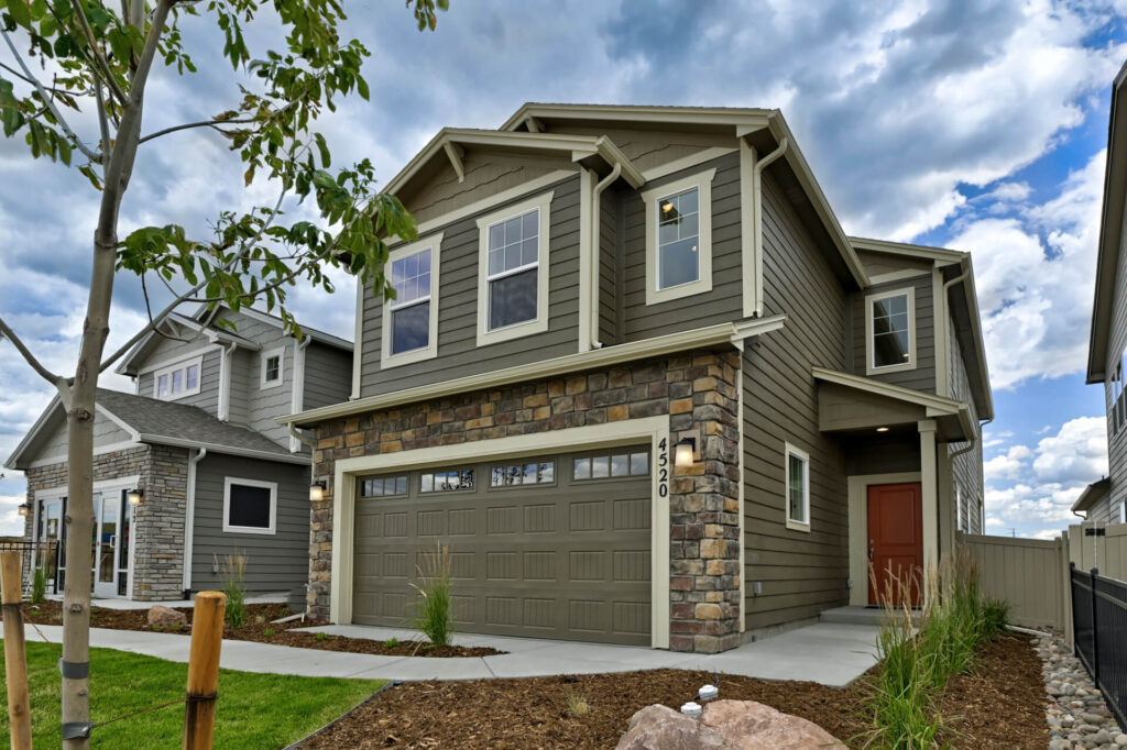 Two-story suburban house with stone-accented garage and green siding under a partly cloudy sky