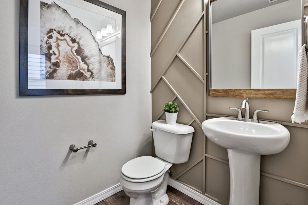 Small half-bath with pedestal sink, toilet, decorative wall trim, and framed artwork