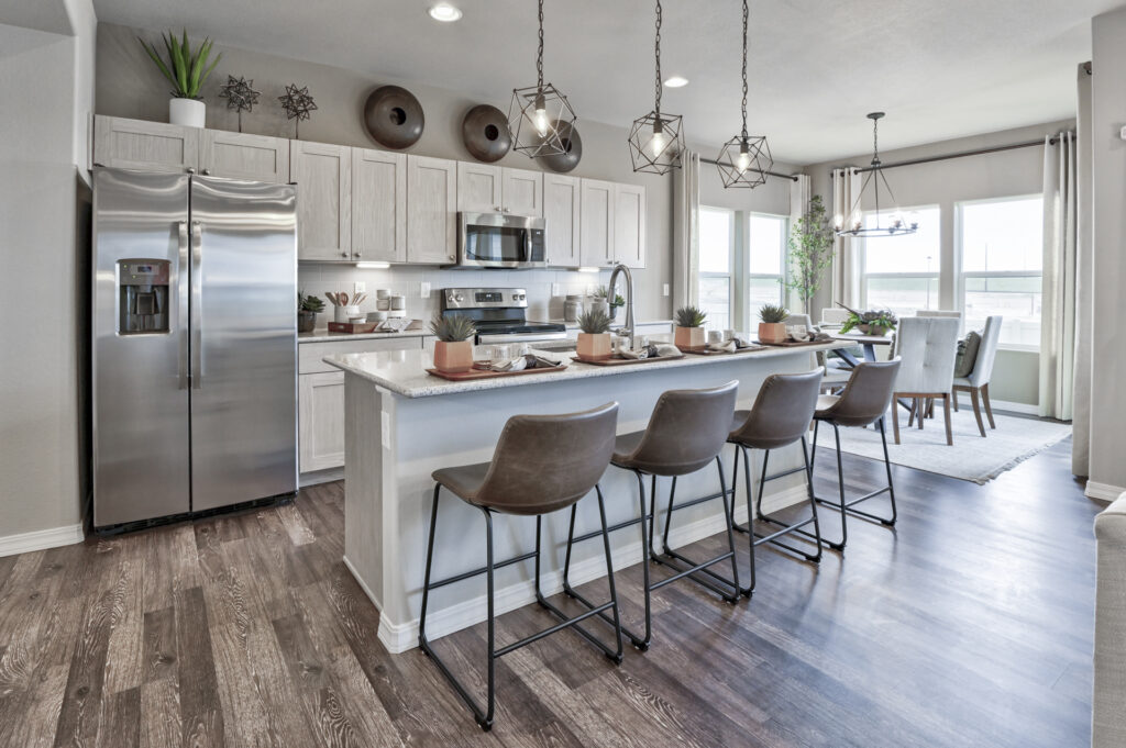 Kitchen with large island, four counter stools, stainless steel refrigerator and pendant lights.