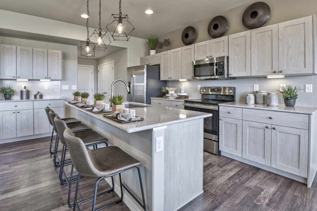 Bright kitchen with long breakfast bar, four stools, oven, microwave, and overhead pendant lights.