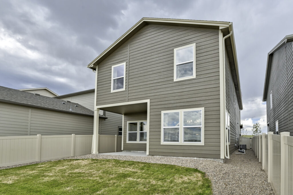 Rear exterior of a two-story house with covered patio, fenced yard, and gravel side paths.