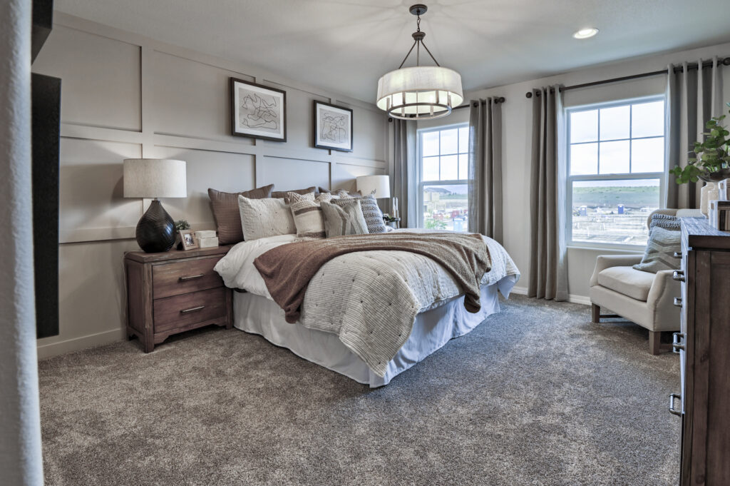 Staged bedroom with bed, nightstands, lamps and two windows under a drum chandelier.