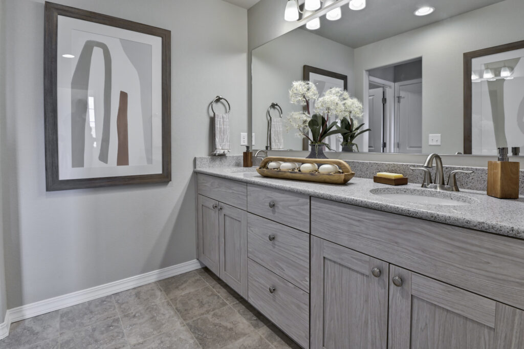 Long bathroom vanity with gray wood cabinets, countertop decor and a framed abstract print on the wall.