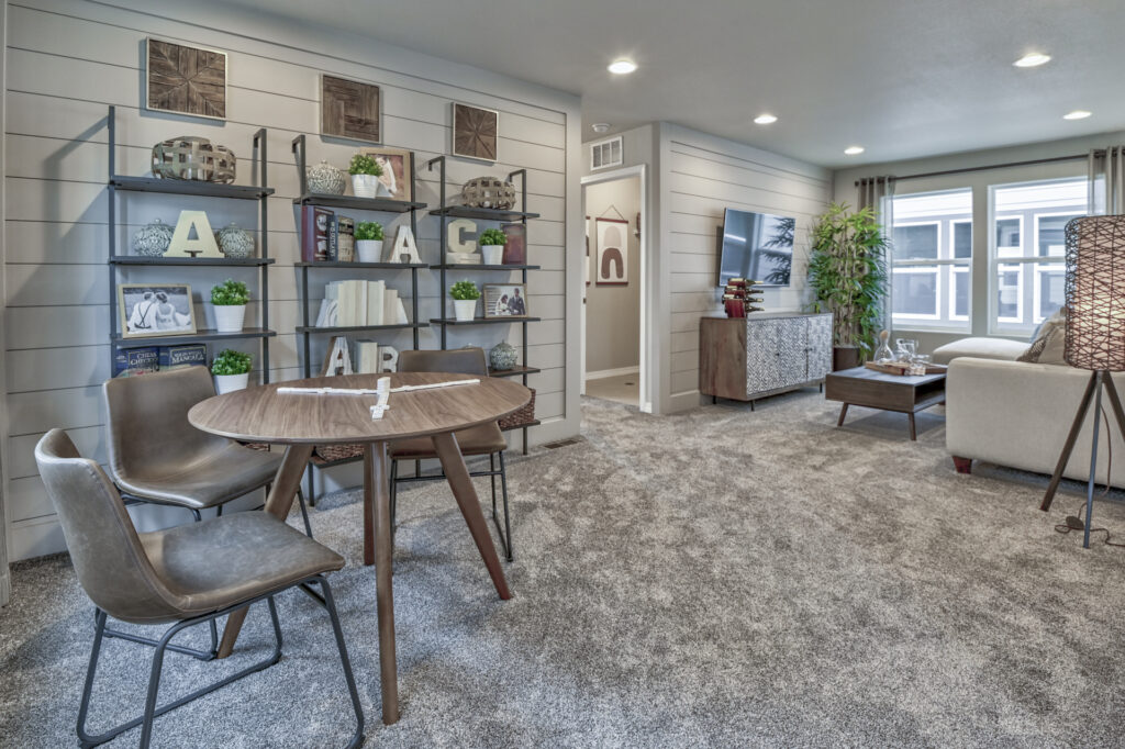 Carpeted living area with round wooden table, shelving unit and seating near a doorway.