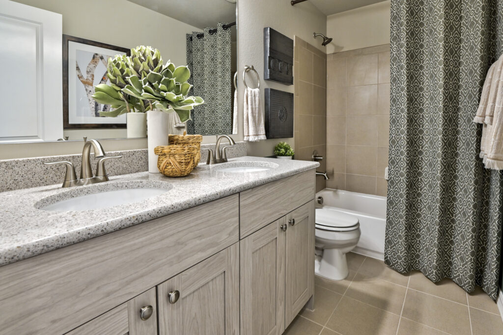 Bathroom vanity with dual sinks, speckled countertop, and a tub with patterned shower curtain.