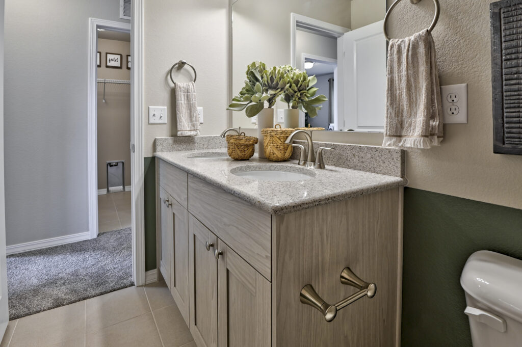Single-sink bathroom vanity with speckled countertop, towel rings, and open doorway to carpeted area.