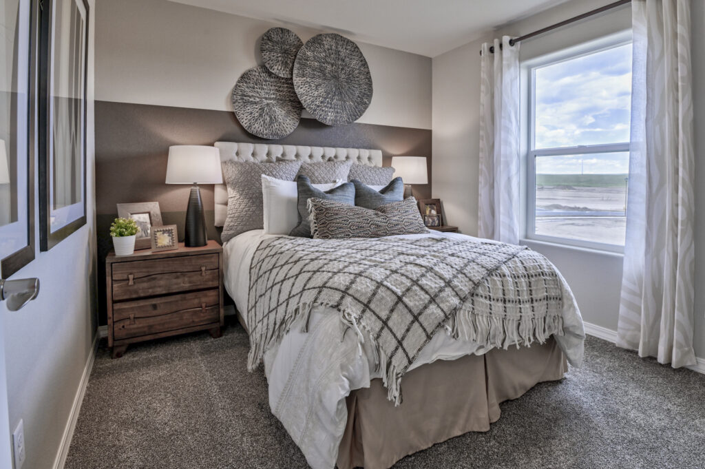 Staged bedroom with a bed, layered pillows and a textured throw, wall decor, and a window.
