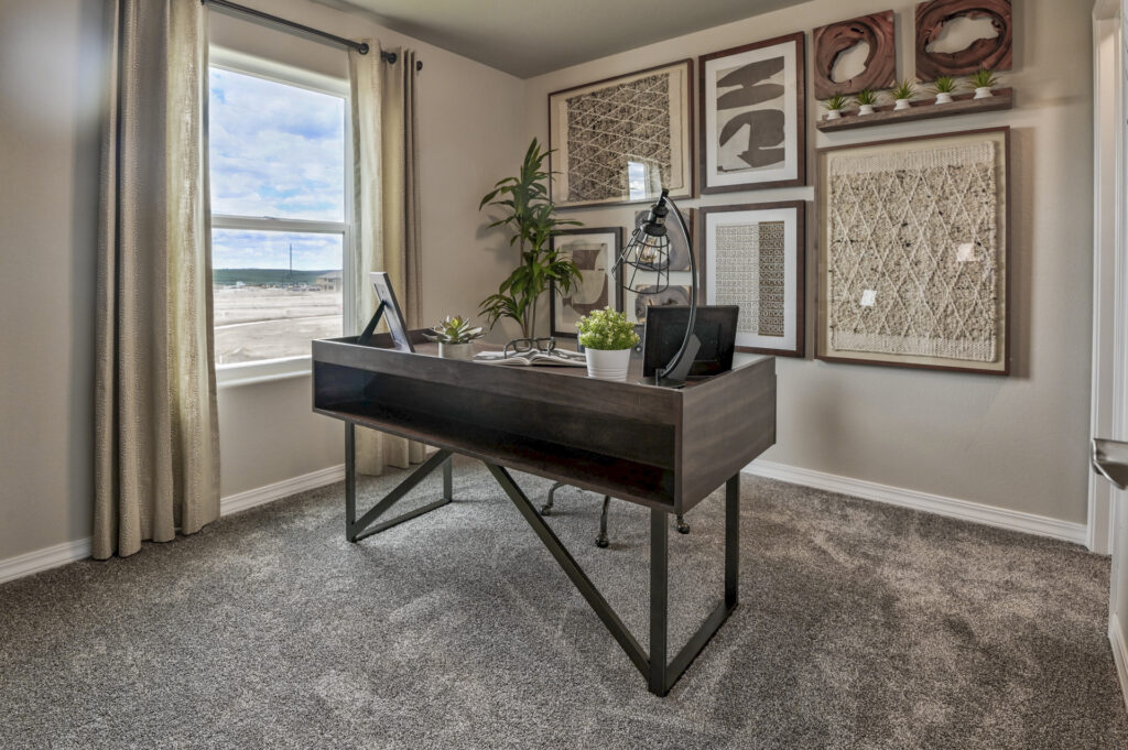 Small home office with dark wood desk, wall art, carpet, and a window with curtains.