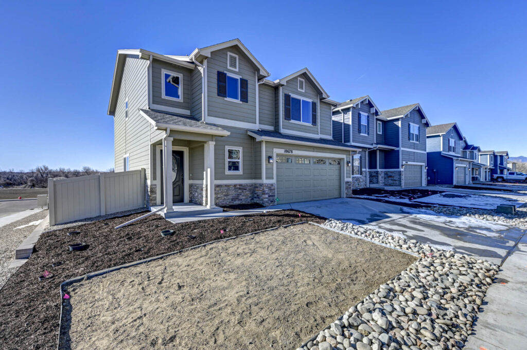 Corner lot two-story townhouse with garage and unfinished front landscaping under clear sky.