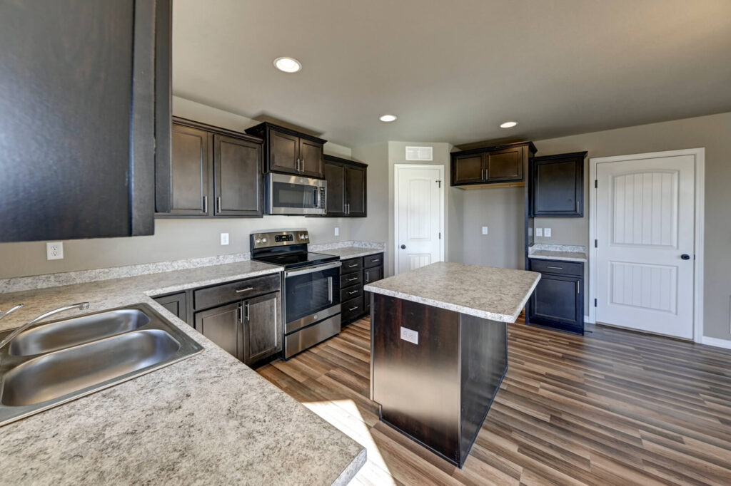 Kitchen from sink perspective showing island, stove, pantry door, and open cabinetry.