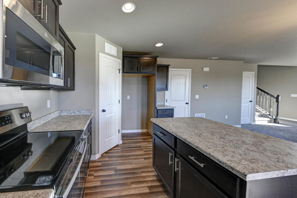 View along kitchen island toward pantry alcove and adjoining living area with stairs.
