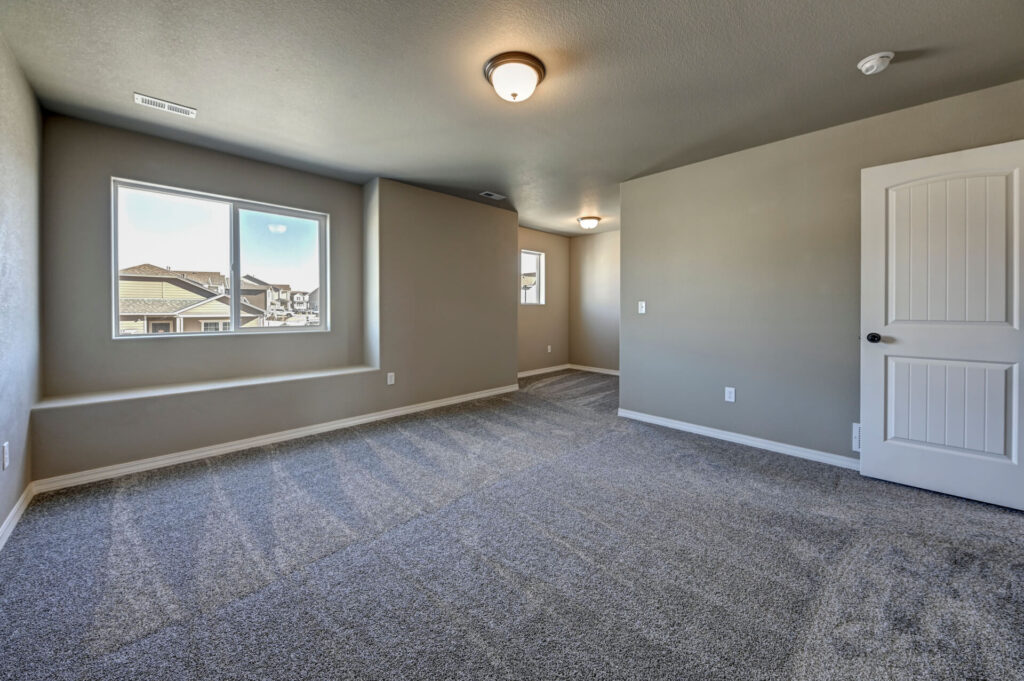 Large carpeted room with window seat, two windows, and a white interior door.