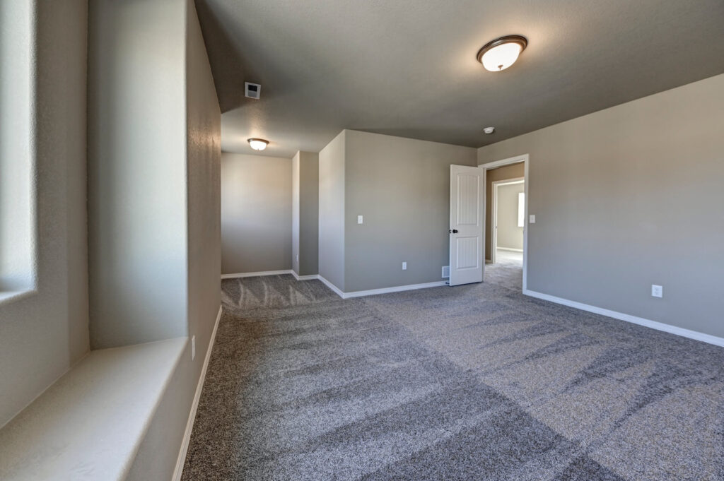 Spacious carpeted room with neutral walls, angled ceiling and window ledge, recessed alcove beyond.