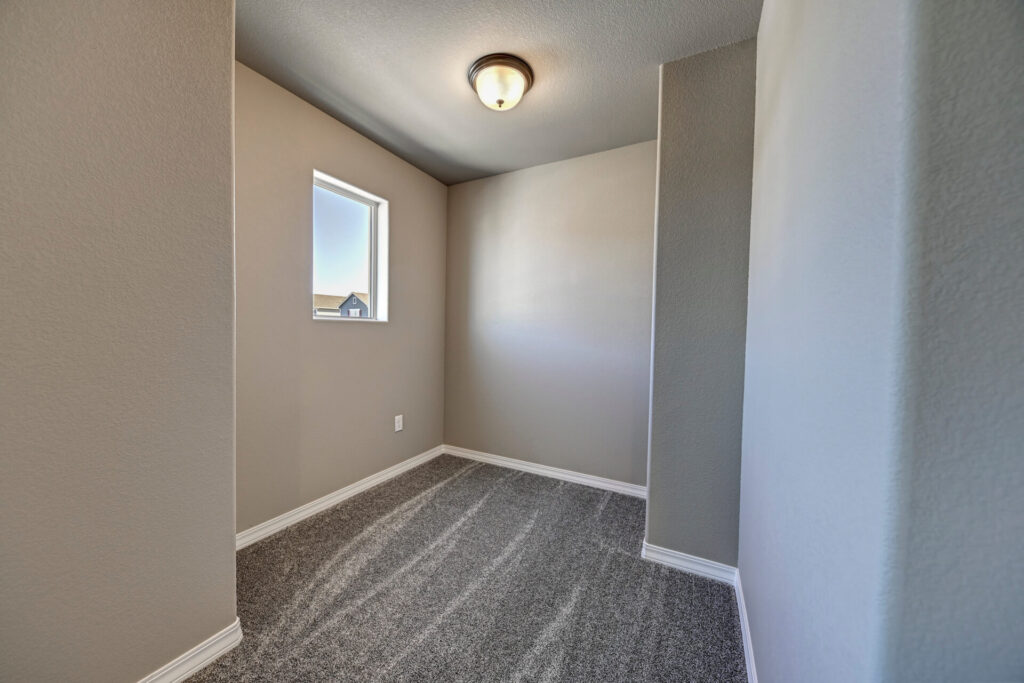 Small carpeted nook or room with one window and flush ceiling light, neutral painted walls.