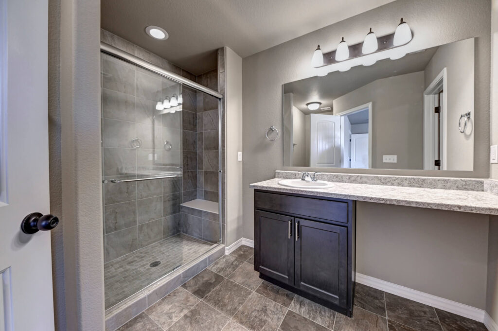 Bathroom with glass-enclosed tiled shower, single-sink vanity and large mirror above.