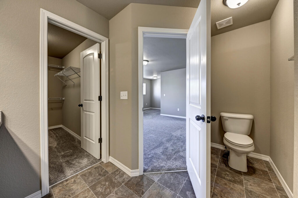 View from bathroom into a bedroom; open closet door on left and toilet in small alcove on right.
