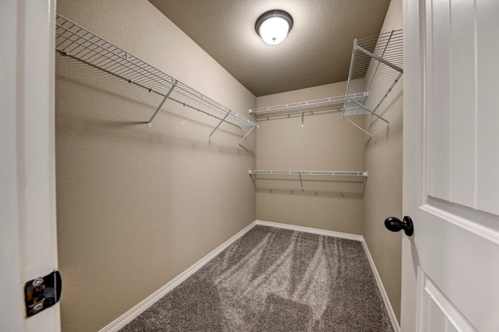 Empty walk-in closet with carpeted floor and multiple wire shelves on three walls.