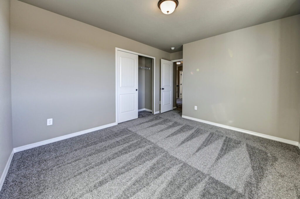 Empty bedroom with open closet door, grey carpet and light fixture centered on ceiling.