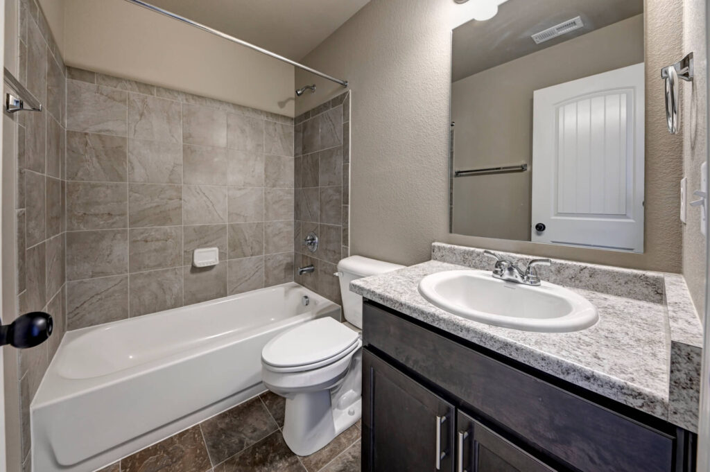 Bathroom with tub-shower combination, tiled surround, vanity sink and mirror.