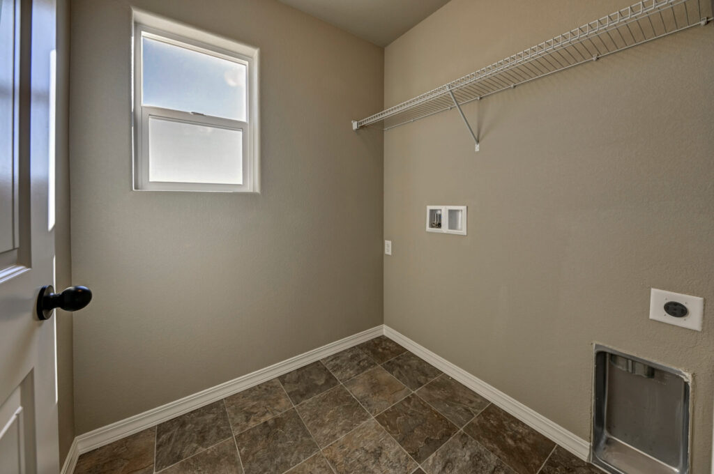 Small laundry or utility room with tiled floor, wall shelf, window, and dryer hookup.