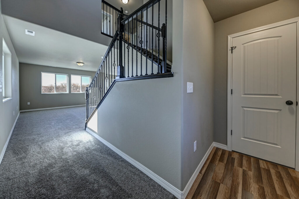 Hallway and stairwell with carpeted floor, metal balusters, and a white interior door.