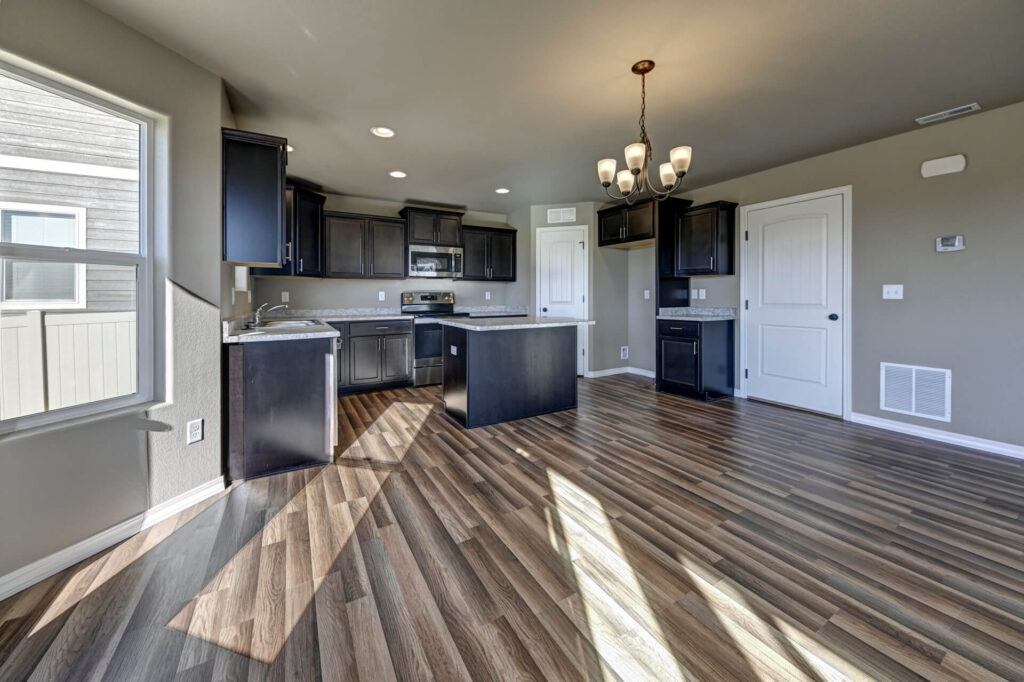 Kitchen and dining area with dark cabinetry, island, chandelier, and wood-look flooring.