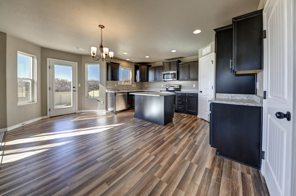 Open kitchen and dining area with island, dark cabinets, wood-look floors, and glass door to outside.