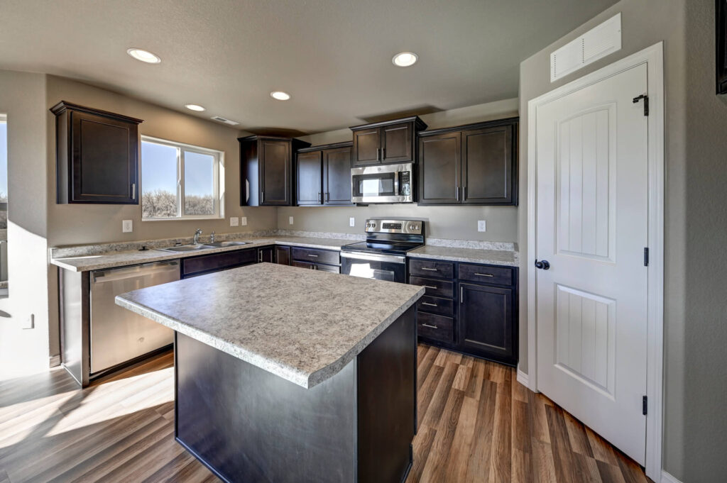 Kitchen island in front of L-shaped counters, dark cabinetry, and a window over the sink.