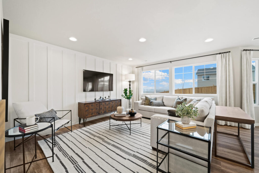 Bright living room with large window, sectional sofa, TV mounted on paneled accent wall.