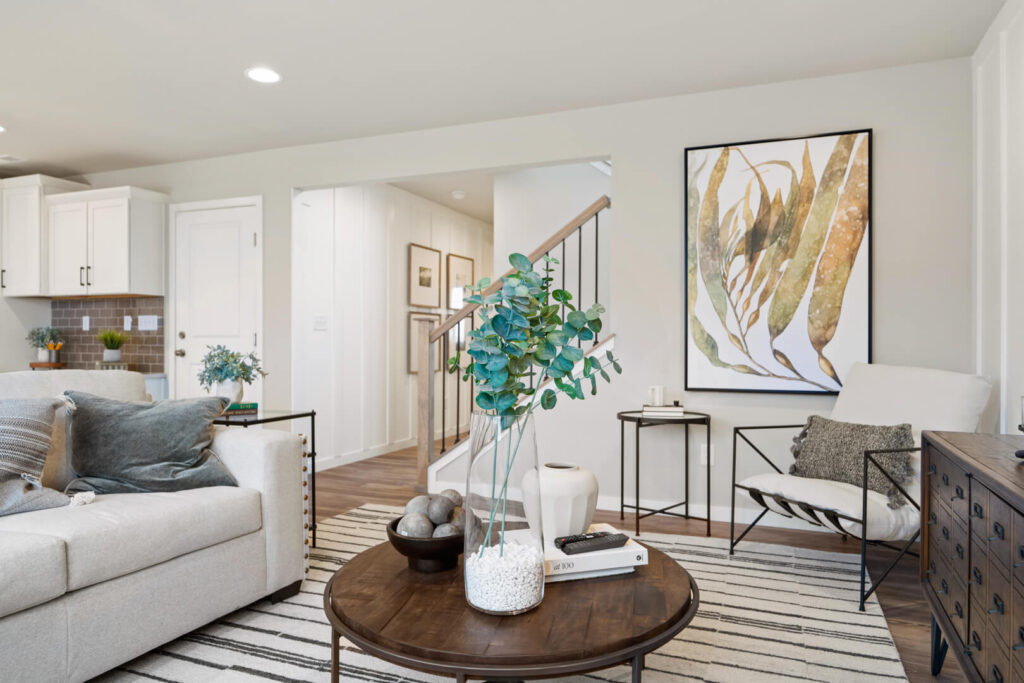 Bright living room with neutral sofa, round wood coffee table, patterned rug, and staircase in background.