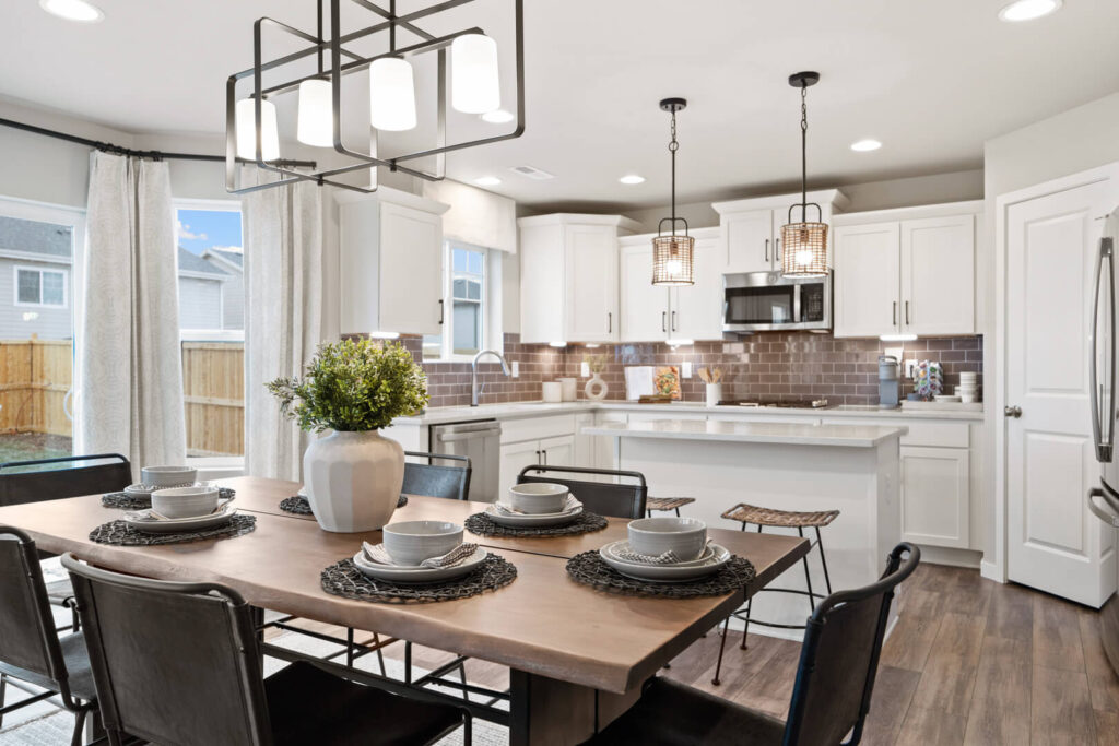 Open dining area and kitchen with wooden table set for four, pendant lights, and sliding door.