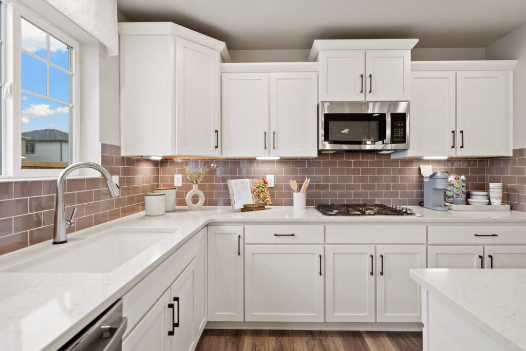 Bright white kitchen corner with undermount sink, quartz counters, subway tile backsplash, and microwave.