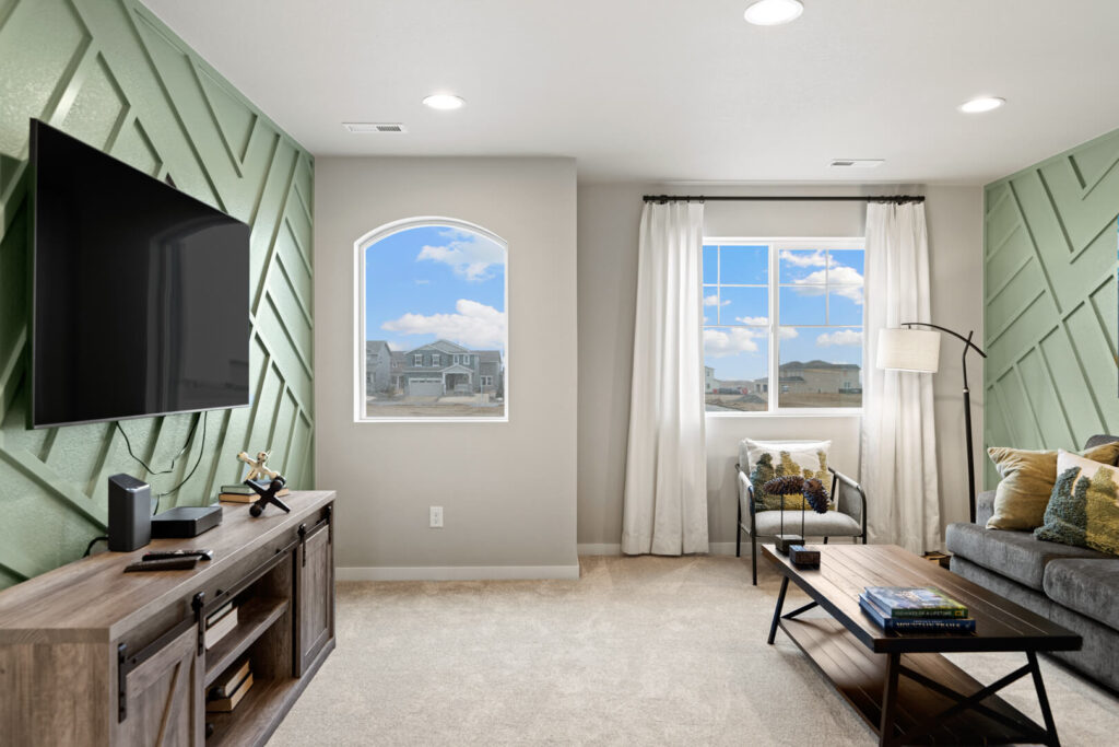 Small living area with wall-mounted TV, green textured accent wall, and two windows showing outside.