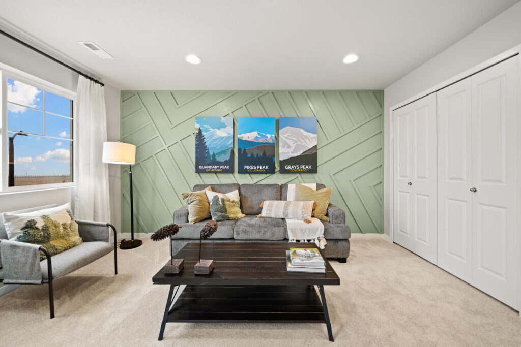 Sofa and armchair in a living room with green paneled accent wall and coffee table holding books.