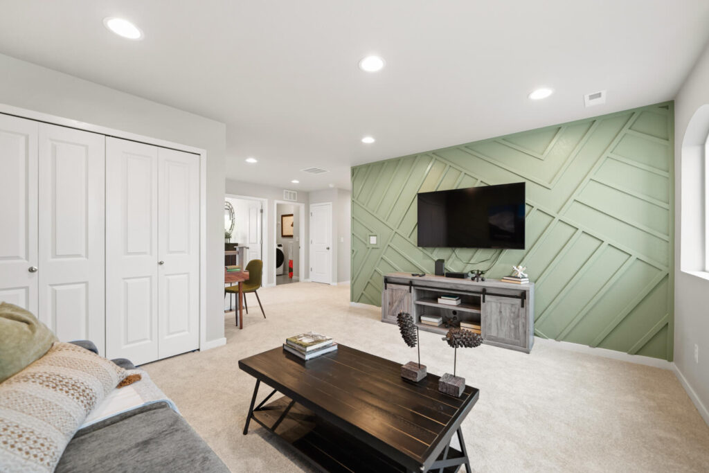 Open family room with TV mounted on a green geometric accent wall and a central coffee table.