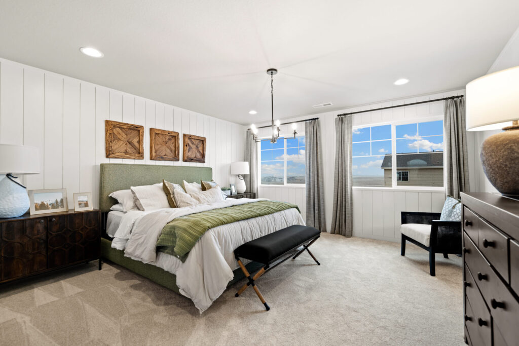 Bright bedroom with green upholstered bed, wood accent art, two windows and neutral carpeting.
