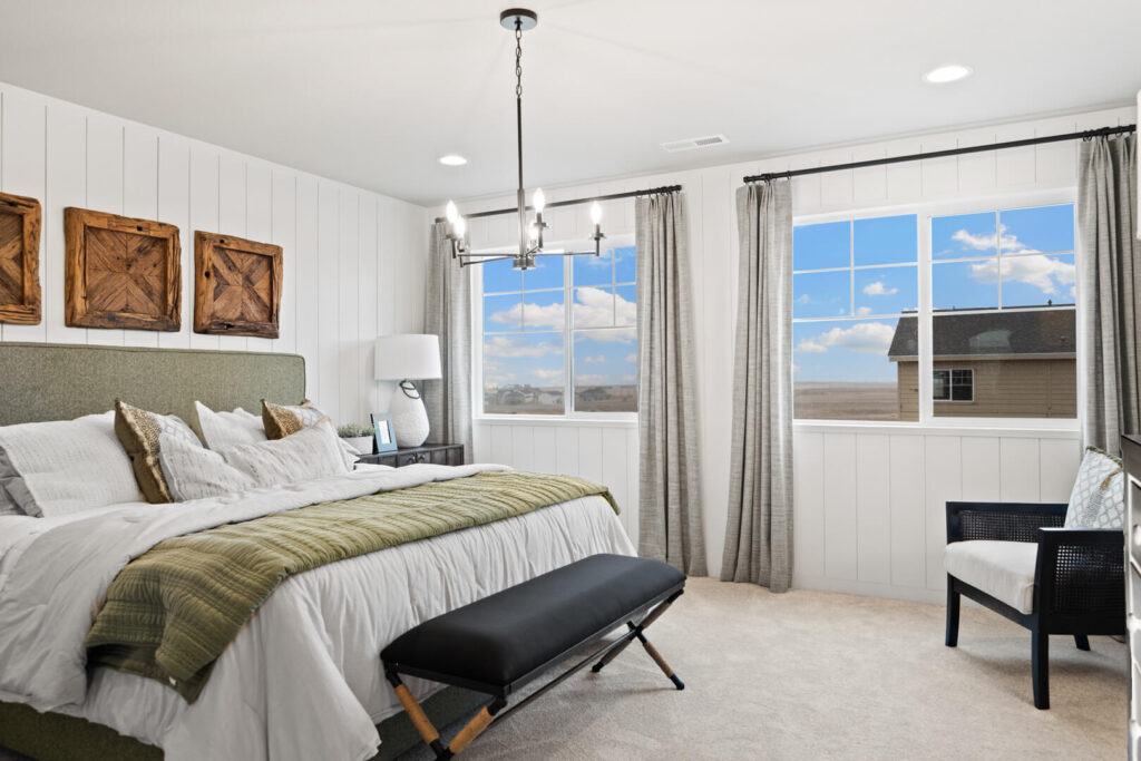Angled view of a staged bedroom showing bed with green throw, chandelier, and two side windows.