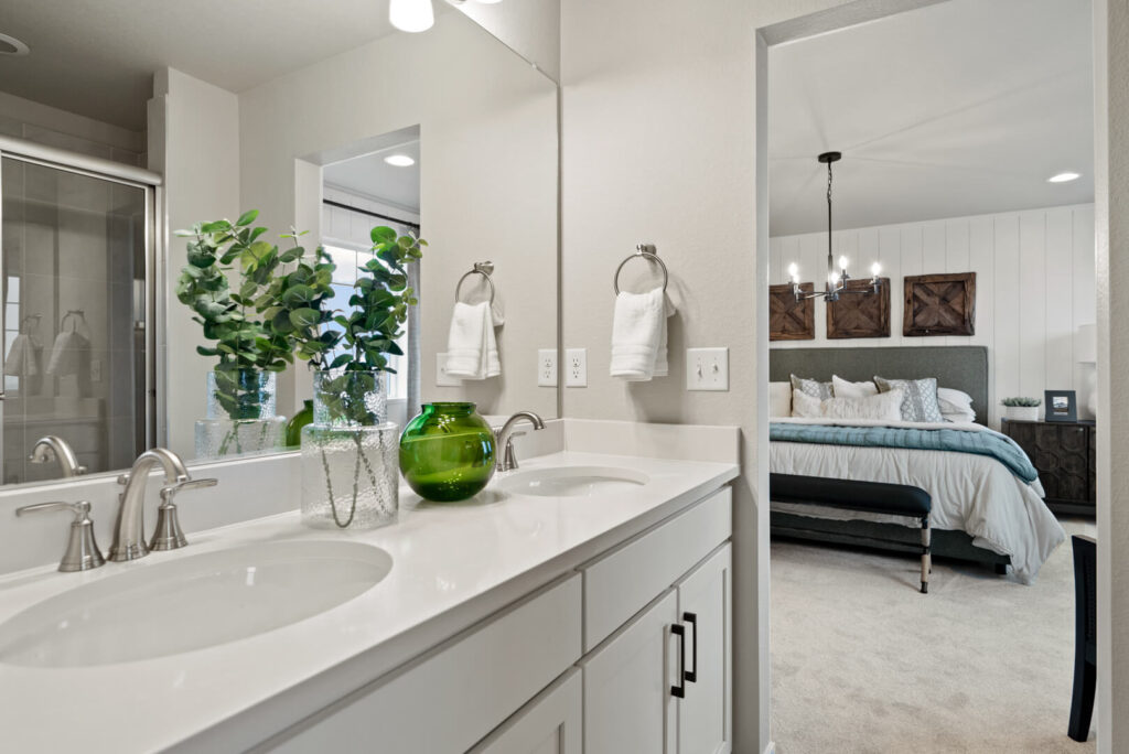 Bathroom vanity reflection showing twin sinks and a view through to an adjacent bedroom.