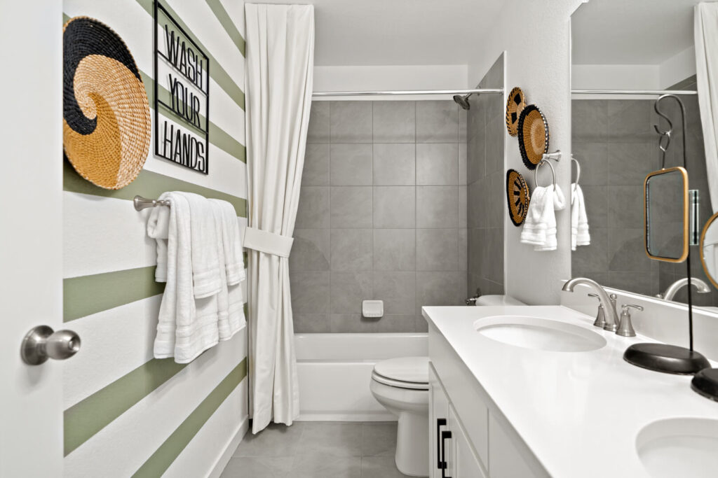 Compact bathroom with striped green-and-white wall, shower-tub, and double-sink vanity.