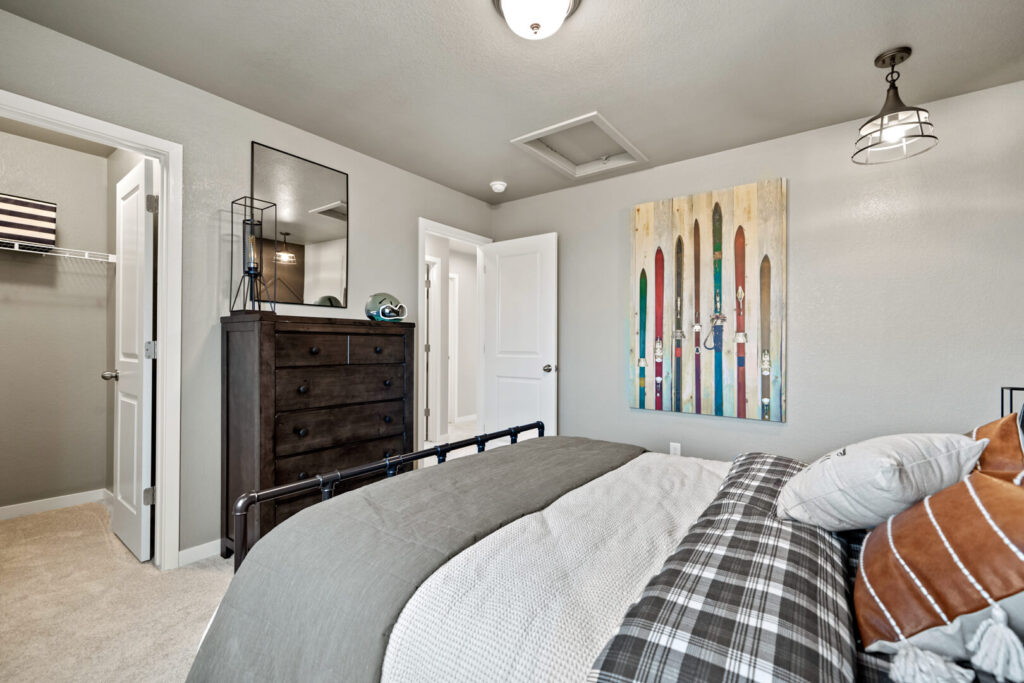 Bedroom view from foot of bed showing dresser, open closet door, and colorful wall art.