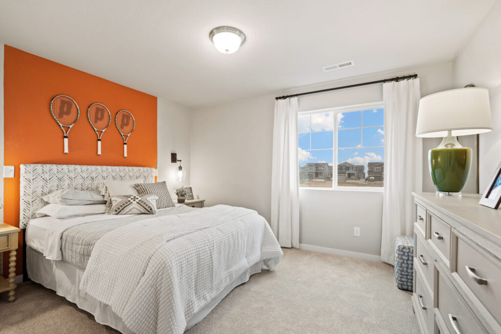 Bright bedroom with white bedding, orange accent wall behind the headboard, and a dresser by the window.