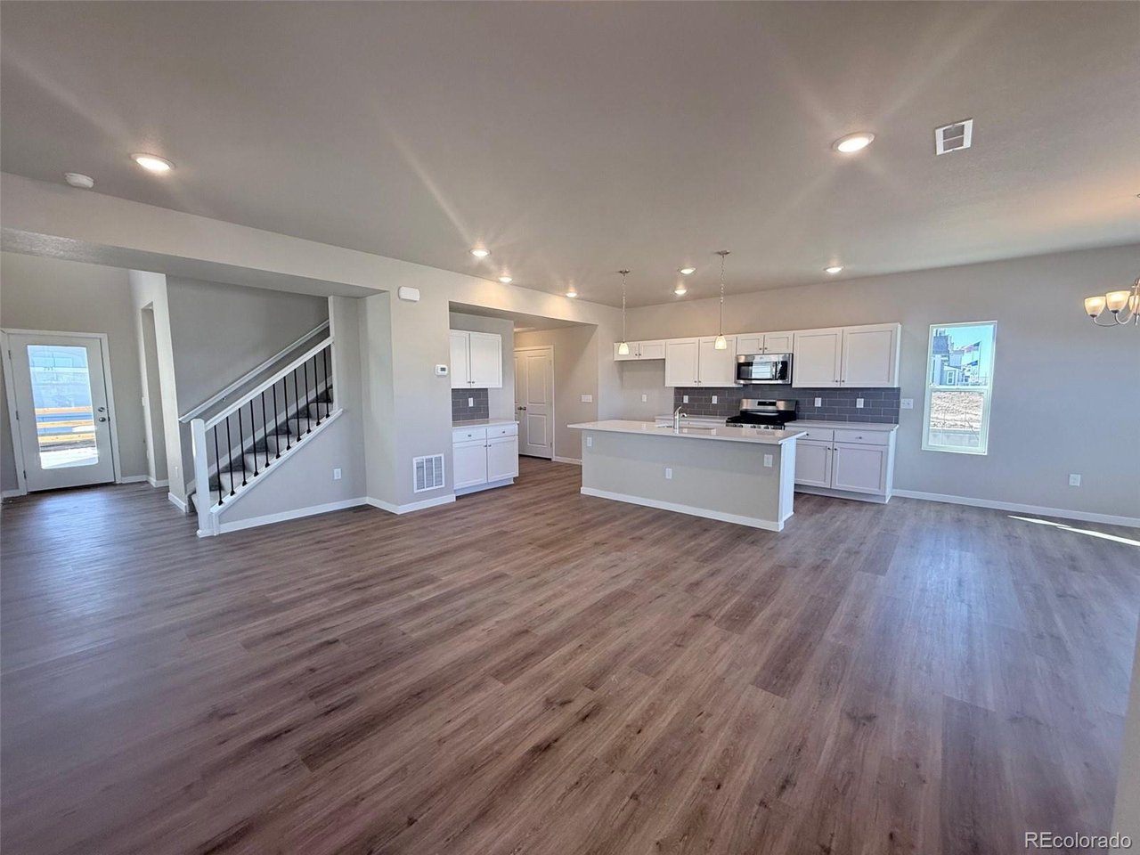 Great room with open-plan kitchen, island counter, pendant lights, and adjacent staircase with black balusters