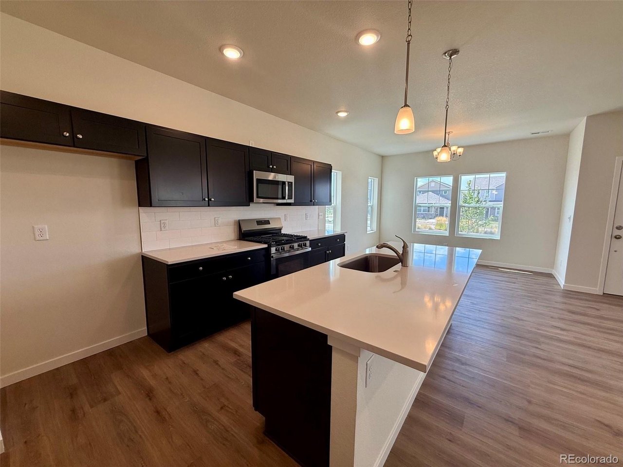 kitchen with dark upper and lower cabinets, center island with sink, pendant lights, and adjoining dining area with three large windows