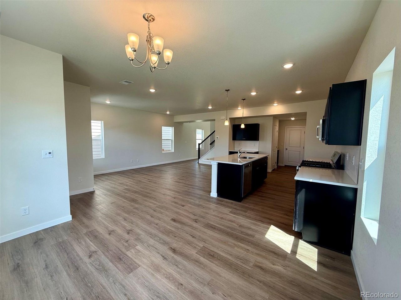 living room and kitchen with open floor plan, island with sink, pendant lights, and vinyl plank flooring