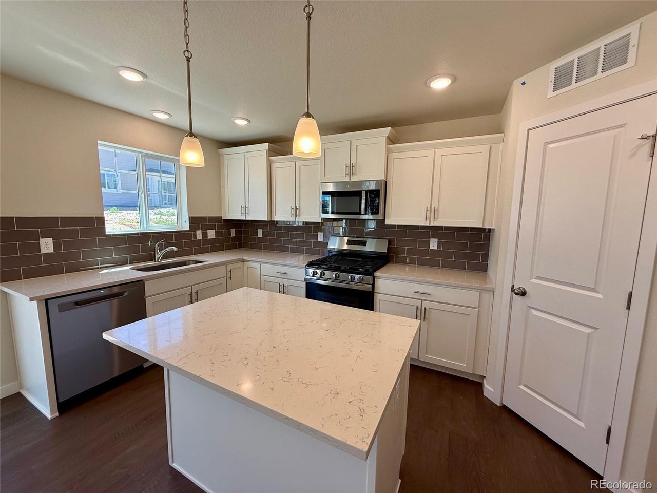 kitchen with central island, white shaker cabinets, dark subway tile backsplash, stainless steel appliances and pendant lights