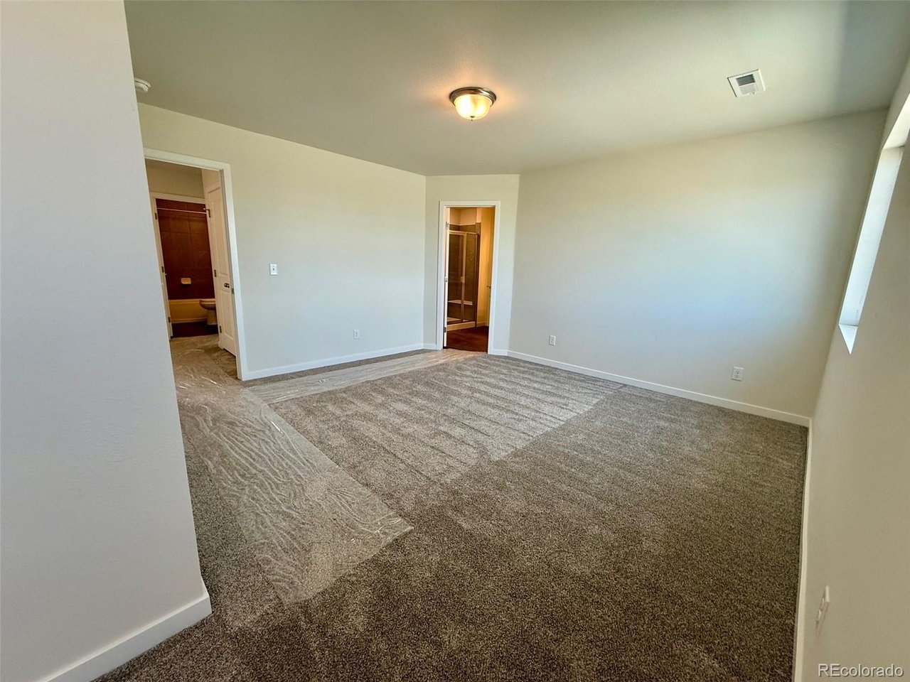 bedroom with carpeted floor, small doorway to an ensuite bathroom and neutral painted walls