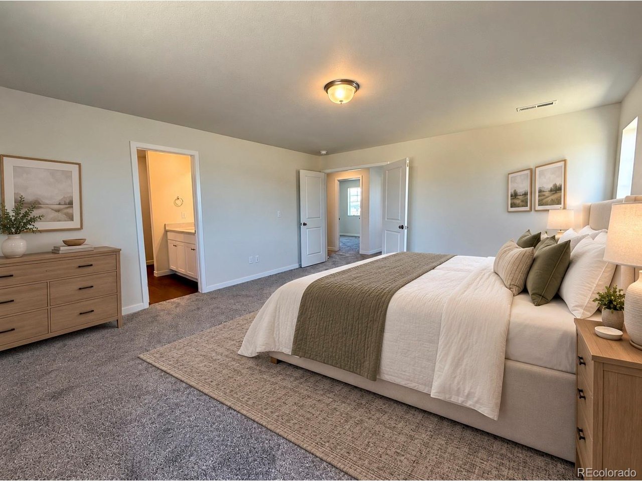 Bedroom with upholstered bed, neutral bedding and green throw, carpeted floor, dresser and open double doors showing an adjacent room and bathroom doorway.